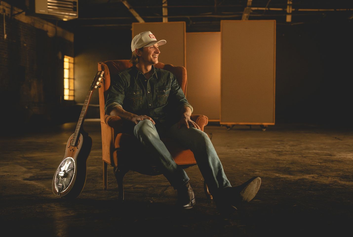 Cooper Alan sat on a chair with a guitar beside him
